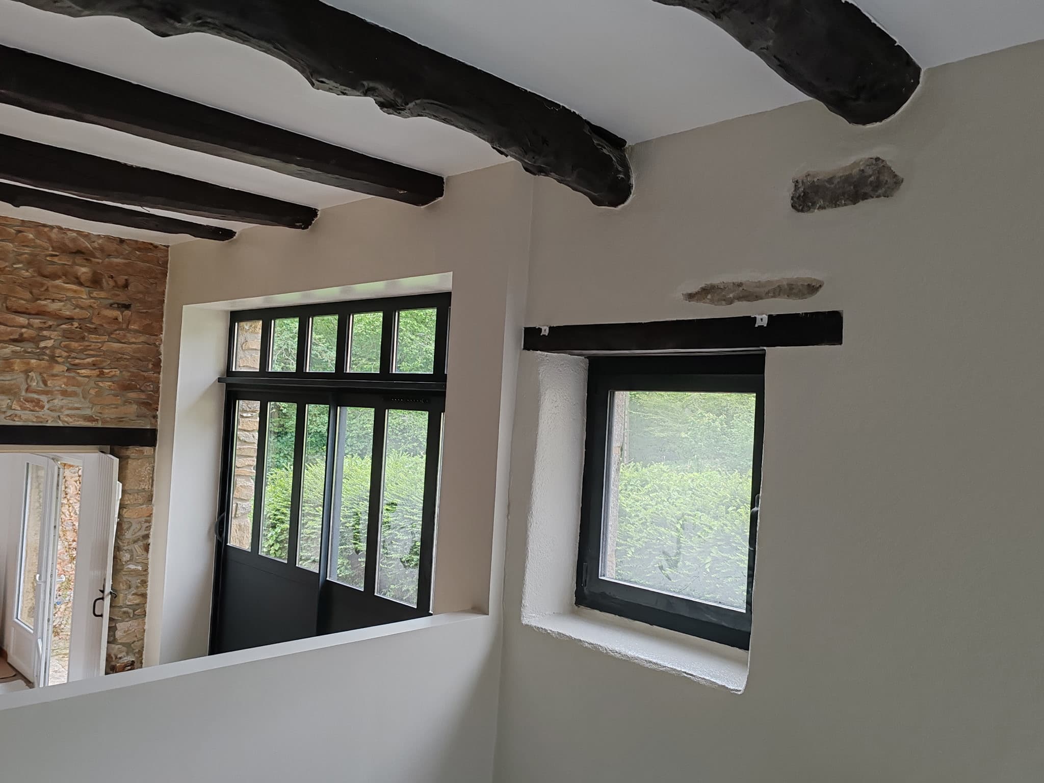 Intérieur ferme rénovée avec verrière noire et pierre apparente