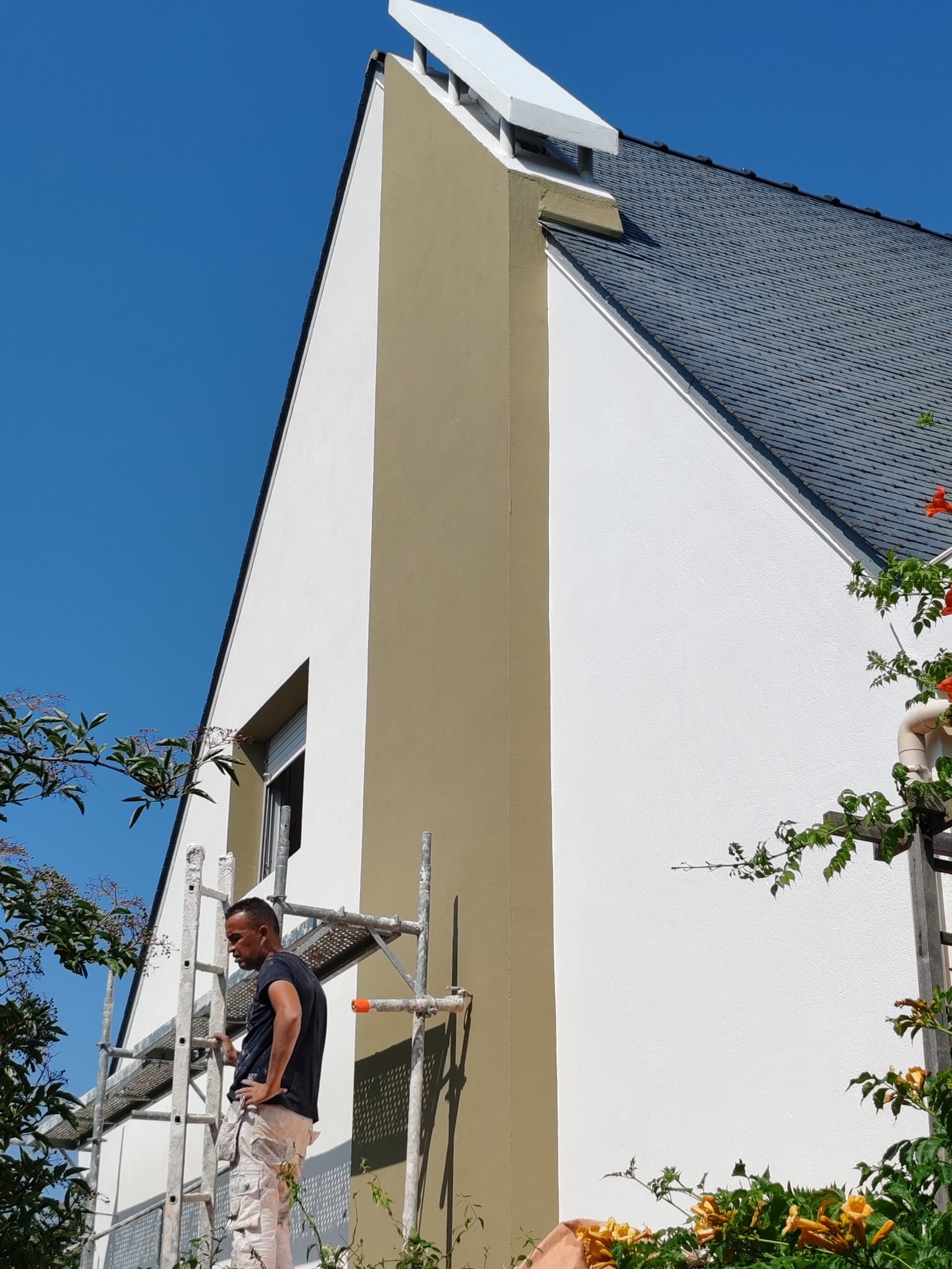 Peintre sur échafaudage devant façade avec pignon peint